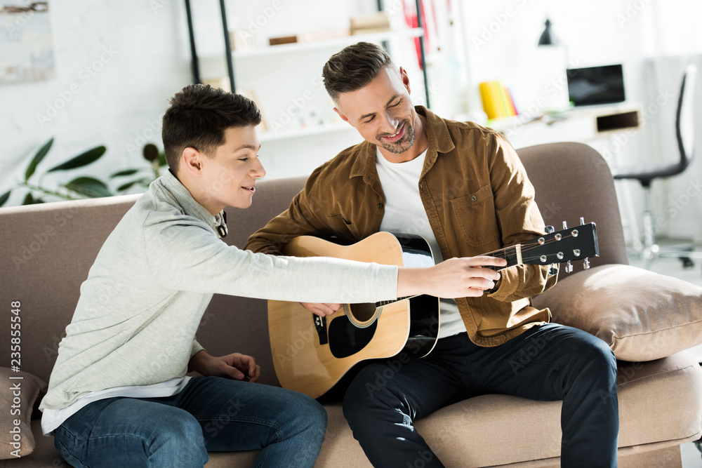 teen son teaching father play acoustic guitar at home