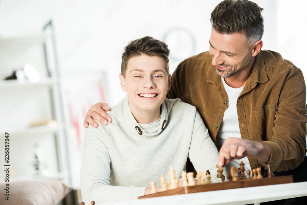 father hugging happy teen son at table with chess at home father hugging happy teen son at table with chess at home