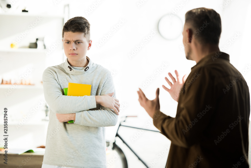 Obraz premium irritated father gesturing and looking at sad teen son at home
