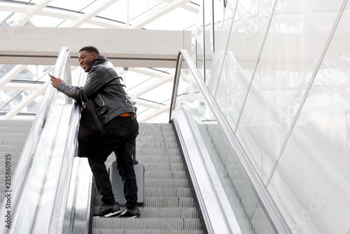young african american travel man on escalator with bags and mobile phone