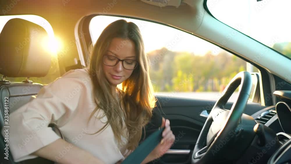 Beautiful girl with glasses inserted wireless headphones into her ears and fastened her seat belt about to drive away in a car
