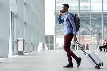 side portrait of young african man traveling with suitcase and cellphone at airport