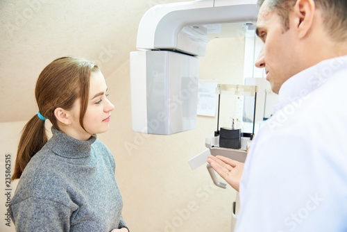 dental tomography. The doctor tells the patient what to do  both are standing next to the scanner.