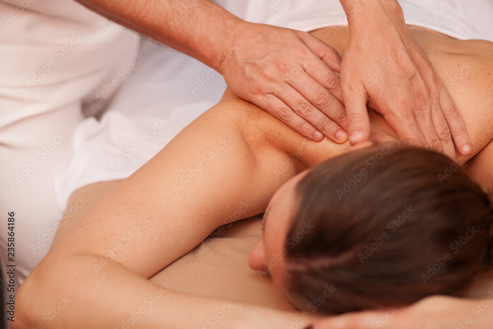 Unrecognizable woman receiving back massage from a professional masseur at the beauty clinic. Spa therapist massaging back of female client. Woman enjoying therapeutic body massage. Skincare, health Unrecognizable woman receiving back massage from a professional masseur at the beauty clinic. Spa therapist massaging back of female client. Woman enjoying therapeutic body massage. Skincare, health