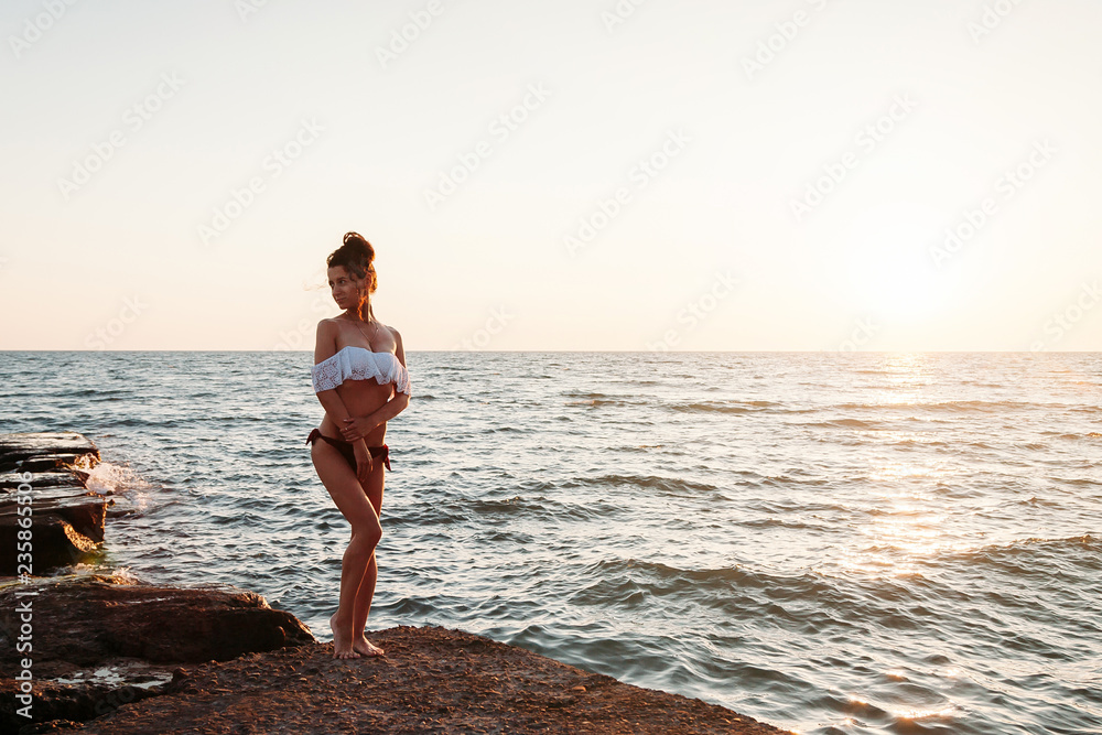 Beautiful young woman posing on beach in front of sunset