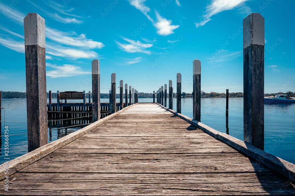 Old wooden pier leading to lake with blue cloudy sky