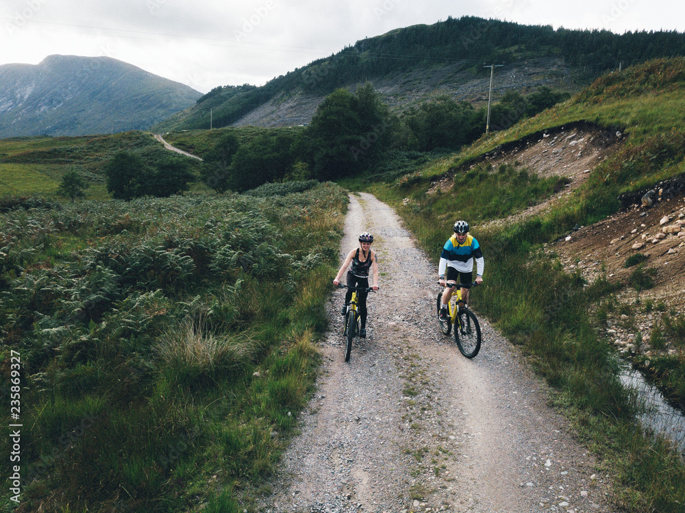Fototapeta premium Couple cycling down a road in the Scottish Highlands