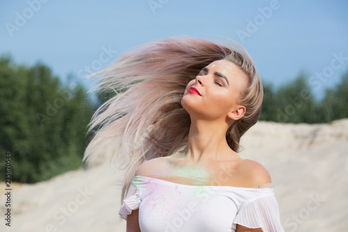 Pretty blonde girl with fluttering hair covered with dry paint Holi at the desert. Empty space
