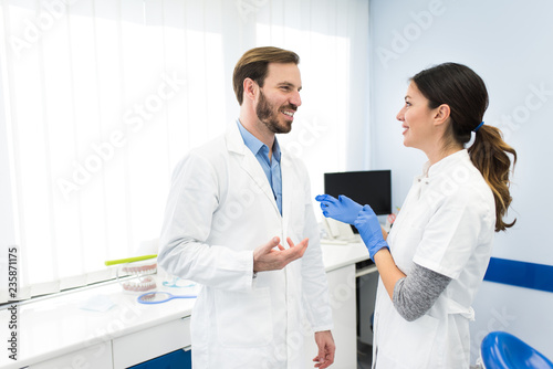Beautiful young dentists talking and smiling, working together as a team in the modern white dentist office. Dentistry concept.