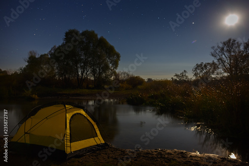 Night sky with stars over the tourist tent by the river. The landscape was photographed on a long exposure.