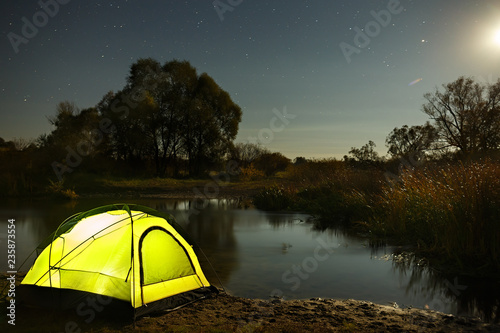 Night sky with stars over the tourist tent by the river. The landscape was photographed on a long exposure.