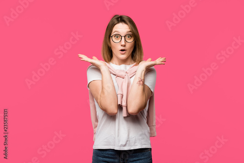 shocked woman in eyeglasses gesturing by hands isolated on pink