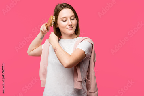 beautiful smiling girl combing hair with hairbrush isolated on pink