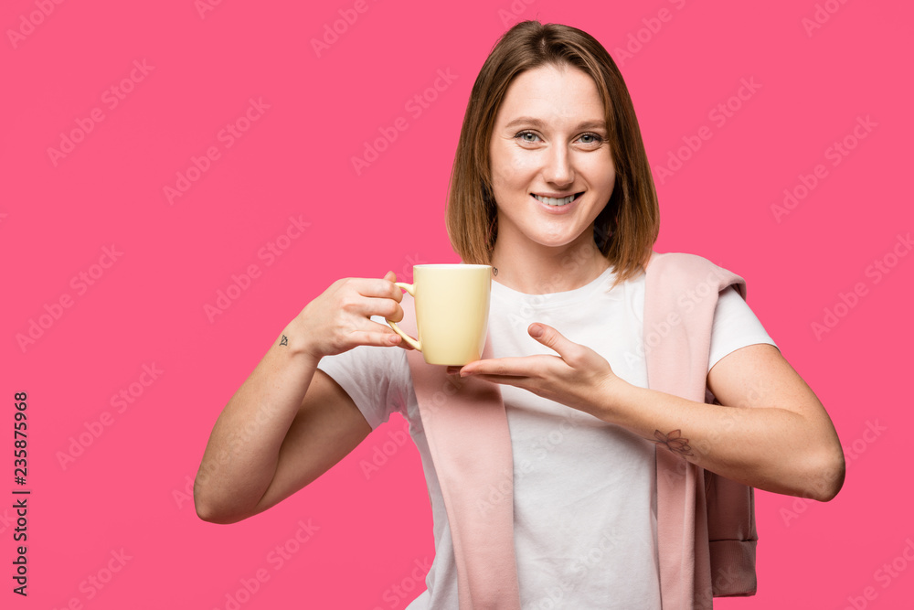 attractive young woman holding cup and smiling at camera isolated on pink attractive young woman holding cup and smiling at camera isolated on pink