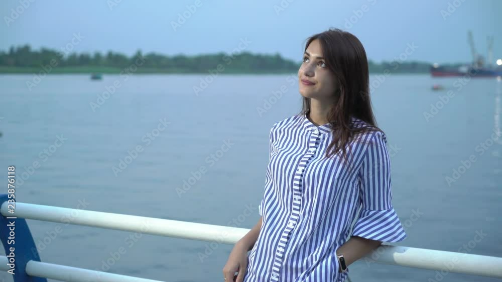 Merry young woman smiling and leaning on the Dnipro quay fence in summer  