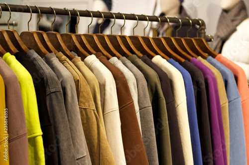 Multicolored outerwear hanging on hangers in the store close-up, side view