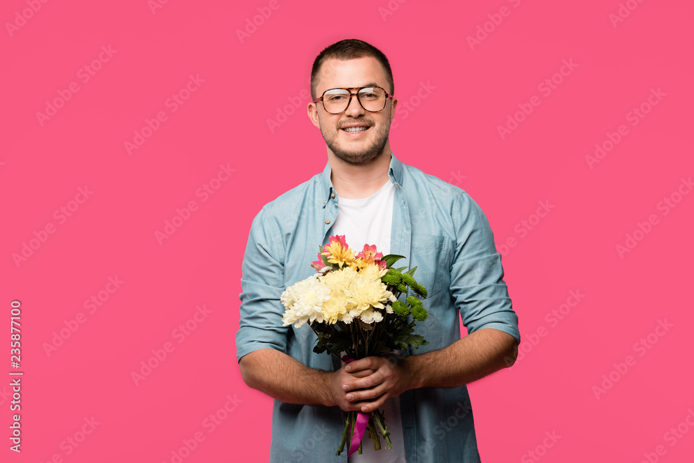 happy young man holding bouquet of flowers and smiling at camera isolated on pink happy young man holding bouquet of flowers and smiling at camera isolated on pink
