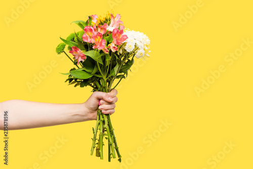 Fototapeta Naklejka Na Ścianę i Meble -  cropped shot of person holding beautiful bouquet of flowers isolated on yellow