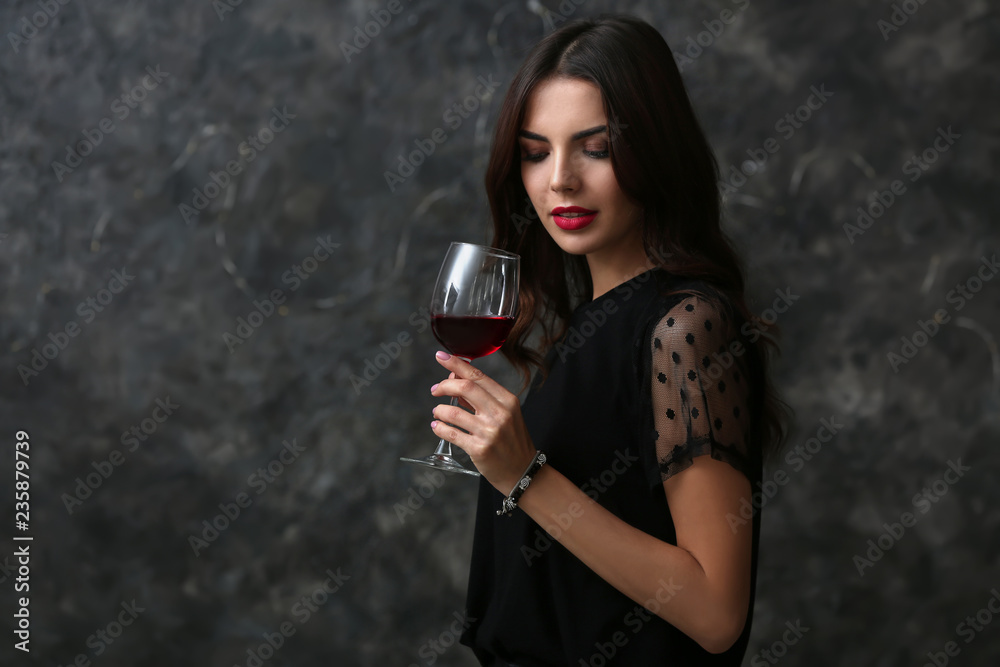 Fototapeta premium Beautiful young woman with glass of wine on dark background