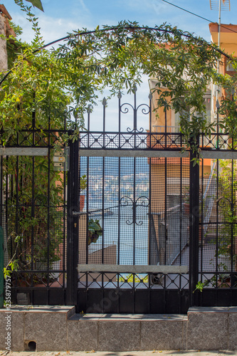 The architecture of Kavala - a beautiful iron gate with climbing plants, through which the harbor is seen. Greece.