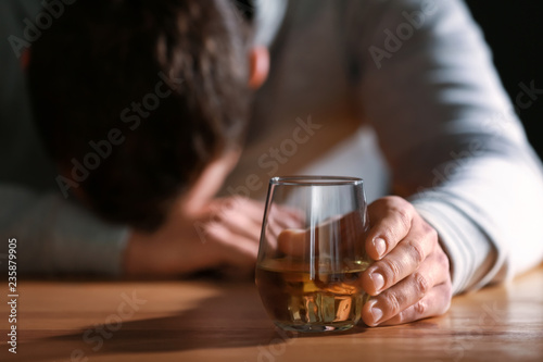 Unconscious drunk man with glass of whiskey at table