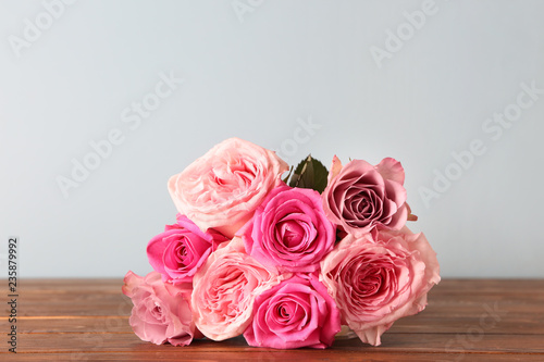 Beautiful bouquet of roses on wooden table against light background