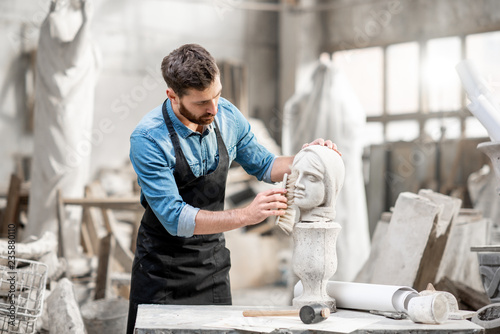 Fotografia Handsome sculptor brushing stone head sculpture on the table in the atmospheric