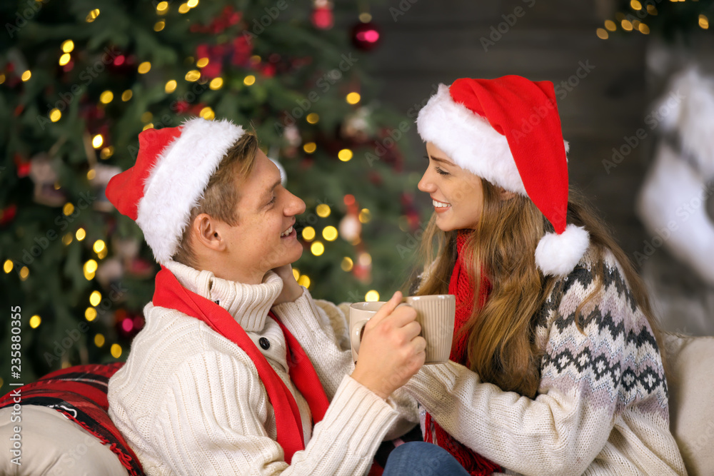 Loving young couple in Santa hats and with hot chocolate celebrating Christmas at home Loving young couple in Santa hats and with hot chocolate celebrating Christmas at home