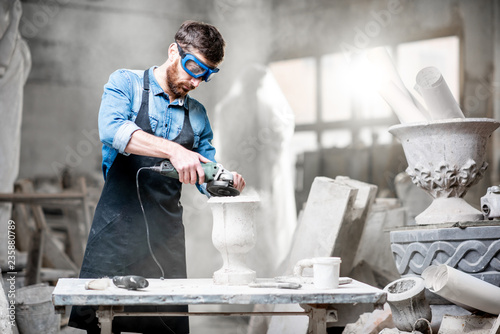 Sculptor in workware grinding stone vase at the working space in the old atmospheric studio photo