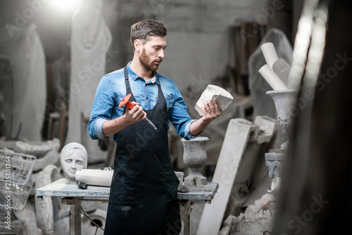 Fotografiet Portrait of a handsome sculptor in blue t-shirt and apron holding old vase in th