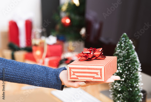 Businesswoman hand holding gift box in christmas holiday at the office with christmas decoration on table.