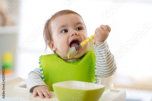 Happy cute infant baby boy spoon eats itself