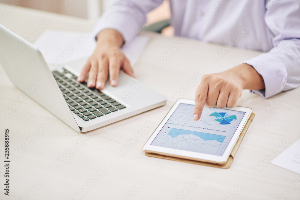 Faceless shot of male worker using laptop and tapping tablet with graphs Faceless shot of male worker using laptop and tapping tablet with graphs