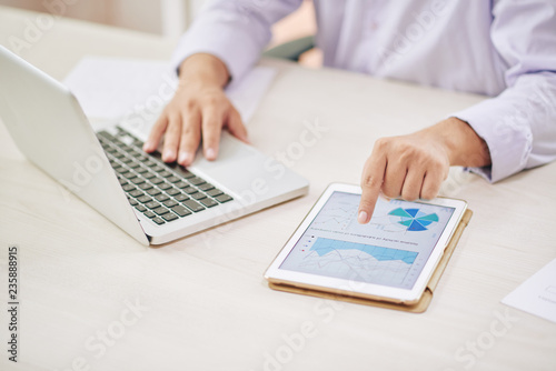 Faceless shot of male worker using laptop and tapping tablet with graphs
