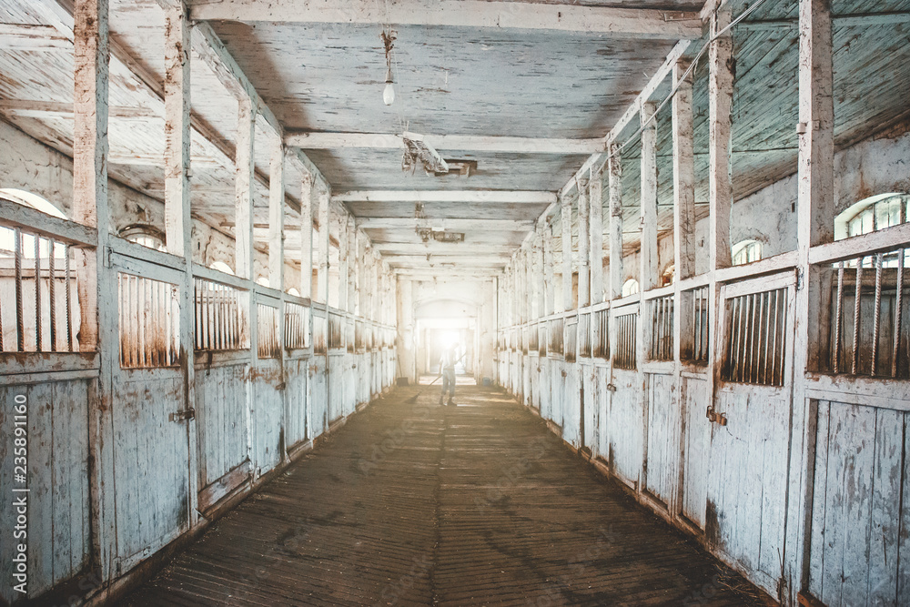 Inside old wooden stable or barn with horse boxes, tunnel or corridor view with light in the end