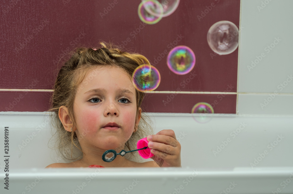 Little adorable baby girl blow bubbles while bathing in the bathroom