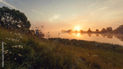 foggy dawn on the river bank with beams of a rising sun