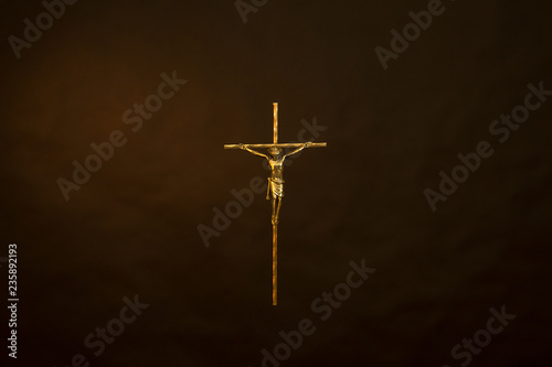 Golden cross with Jesus Christ against smokey black background.