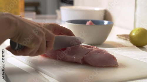 Close-up woman cuts chicken with a knife on a Board. Female hands chef cutting raw chicken meat breast. photo