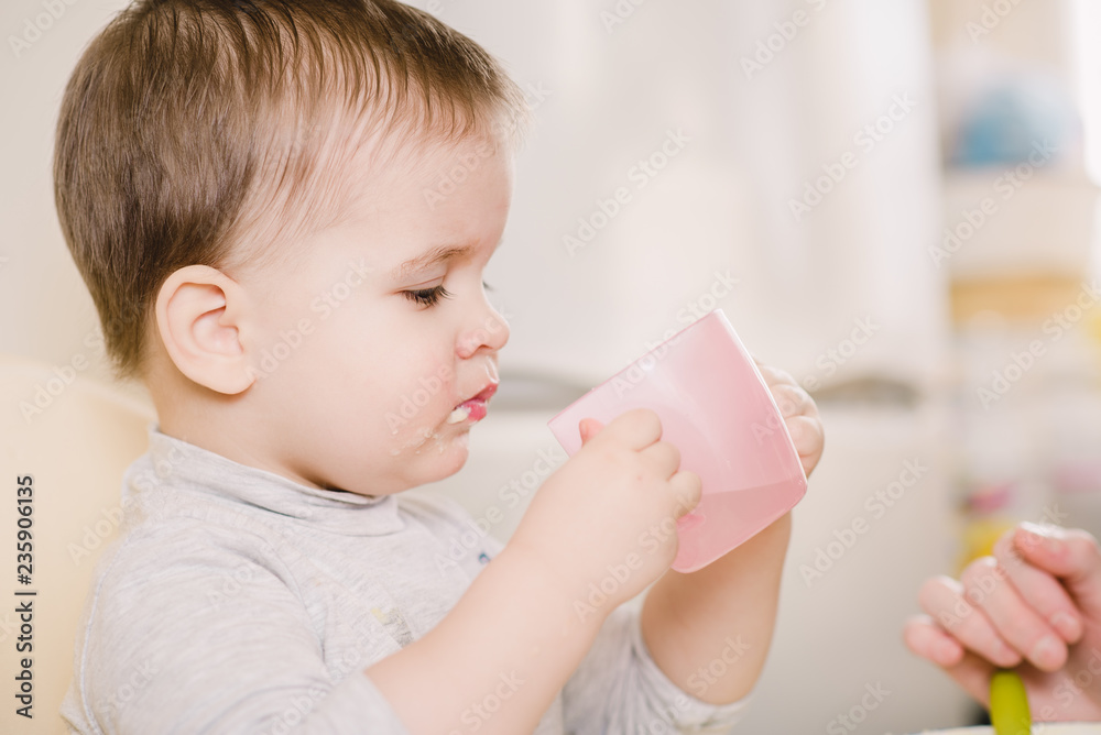 child in the kitchen drinking from a cup of water child in the kitchen drinking from a cup of water