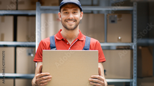 Handsome Warehouse Worker in Uniform Holds Cardboard Box Package and Smiles. photo