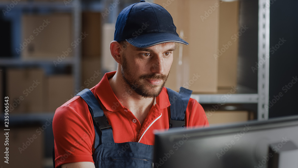 Portrait of Uniformed Worker Using Personal Computer while Sitting at His Desk in the Warehouse. Portrait of Uniformed Worker Using Personal Computer while Sitting at His Desk in the Warehouse.