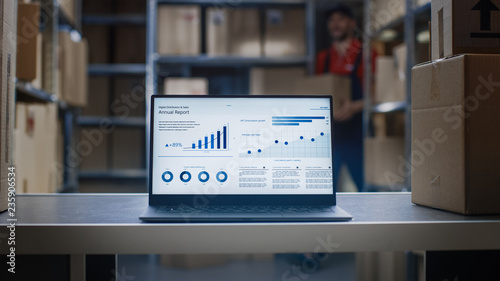 Laptop Screen with Infographics Displaying Graph and Statistics with Annual Results Growth Standing in Warehouse.  photo