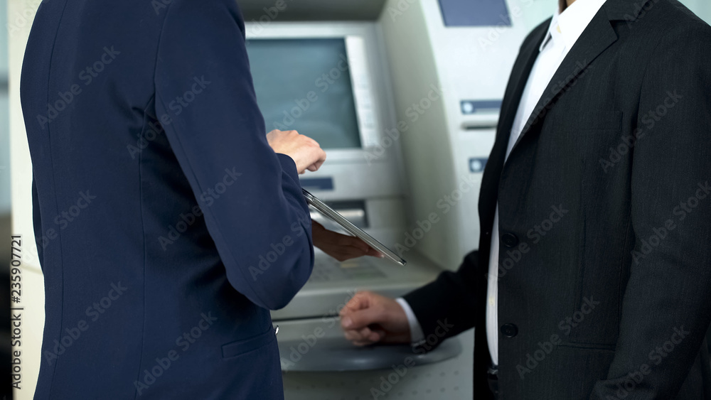 Bank employee showing client on tablet how to withdraw cash and pay bills online Bank employee showing client on tablet how to withdraw cash and pay bills online