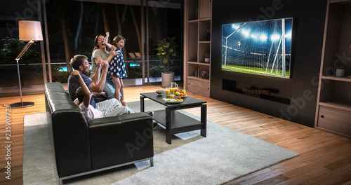 A family is watching a soccer moment on the TV and celebrating a goal  sitting on the couch in the living room.