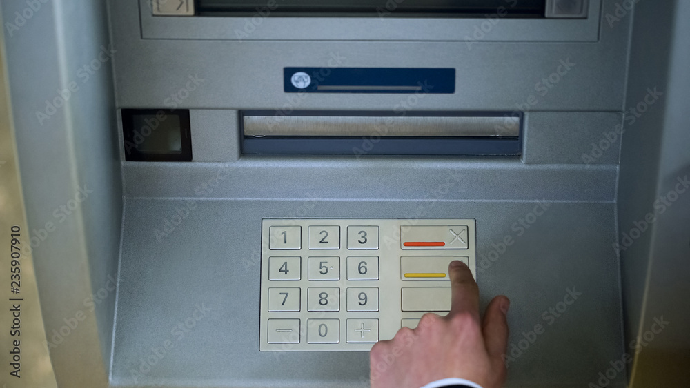 Man correcting pin code on ATM keyboard, transfer funds between bank accounts Man correcting pin code on ATM keyboard, transfer funds between bank accounts