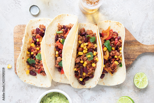 Mexican tacos with meat, beans, tomatoes, corn, paprika and cilantro on wooden board on shabby background.