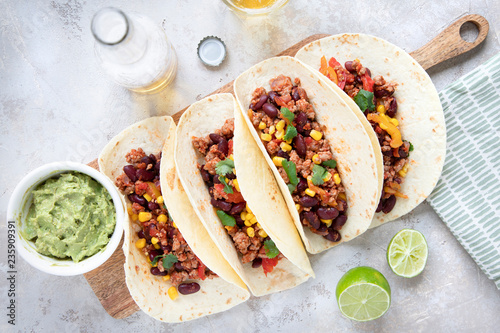 Mexican tacos with meat, beans, tomatoes, corn, paprika and cilantro on wooden board on shabby background.