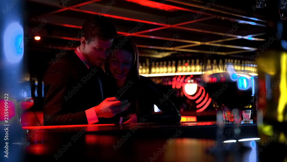 Young happy couple watching pictures on phone in bar, having fun together Young happy couple watching pictures on phone in bar, having fun together