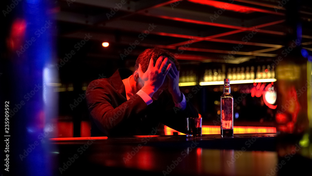 Lonely businessman drinking whiskey in bar, rubbing head, problems on work